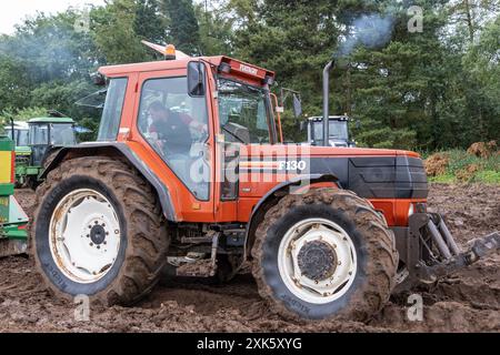 Ballymena, Nordirland - 20. Juli 2024: Rallye für Traktoren und Dampflokomotiven, FIAT AGRI F130 in orange-roten Farben gegen schweren Schlamm. Stockfoto