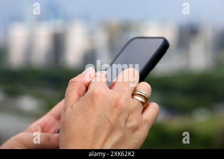 Weibliche Hände mit Smartphone nähern sich verschwommenem Hintergrund von Stadtgebäuden. Frau, die im Sommer das Handy benutzt Stockfoto
