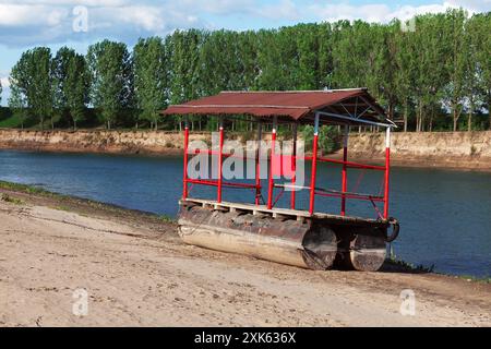 Kleines Boot am Fluss geparkt. Rotes Boot mit Dach sitzt am Strand neben einem Fluss Stockfoto