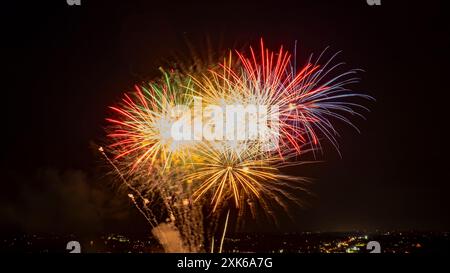 Leuchtendes Feuerwerk in Rot, Grün und weiß platzt am Nachthimmel und schafft Eine lebendige und festliche Atmosphäre über der beleuchteten Stadt. Stockfoto