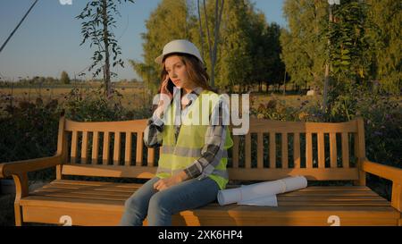 Kaukasische Frau weibliche Öko-Ingenieurin Geschäftsfrau Uniform Schutzhelm Talk Besprechen Sie Geschäftsanruf Mobiltelefon Smartphone-Gespräch Stockfoto
