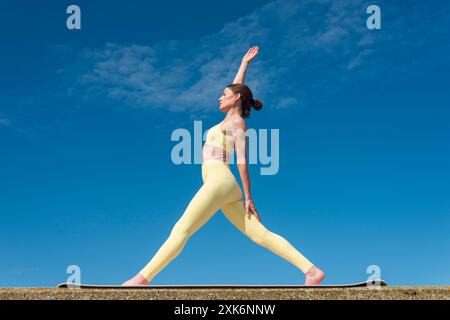 Sportliche Frau, die eine umgekehrte Dreieck-Yoga-Pose im Freien macht, gelbe Sportbekleidung Stockfoto
