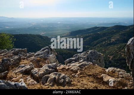 Ein atemberaubender Panoramablick auf eine üppig grüne Bergkette und ausgedehntes Ackerland, von einer felsigen Klippe unter einem klaren blauen Himmel aus gesehen. Stockfoto