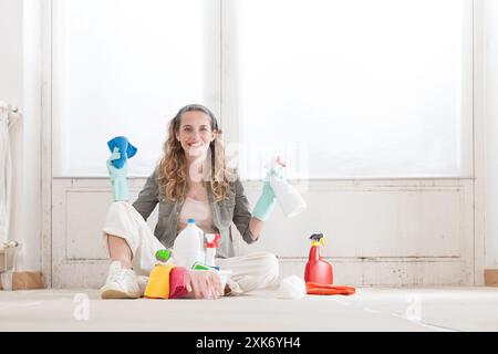 Eine glückliche lächelnde Frau mit Haushaltsreinigungsprodukten zur Schimmelbeseitigung an der Fensterwand zu Hause. Mit Handschuhen und sie putzt mit dem Sprühbot auf Stockfoto