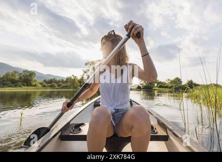 Fröhlich lächelnde Frau, die an einem schönen, ruhigen, sonnigen Sommertag auf einem See Kanu fährt, Nahaufnahme. Urlaubs- und Freizeitkonzepte. Stockfoto