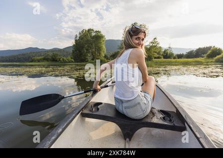 Entspannende Kanufahrt, eine Frau, die an einem angenehmen Sommertag auf dem malerischen See Kanu fährt. Naturliebhaber und aktive Lebenskonzepte. Stockfoto
