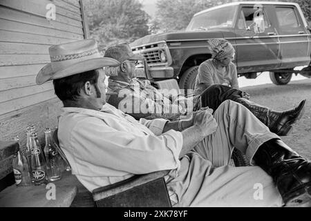 Mazedonien, Arkansas, Vereinigte Staaten – 27. Juni 2024: Horizontale Aufnahme von drei Freunden, die vor einem alten Laden sitzen. Stockfoto