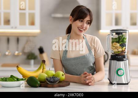 Junge Frau, die leckeren Smoothie mit Mixer am weißen Marmortisch in der Küche zubereitet Stockfoto