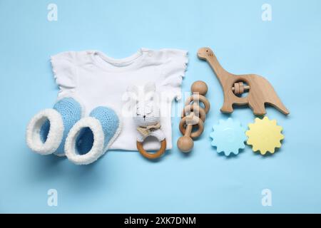 Hölzerne Rasseln, Babyhemd und gestrickte Stiefeletten auf hellblauem Hintergrund, flacher Lay Stockfoto