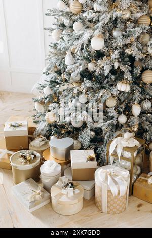 Wunderschön gewickelte Weihnachtsgeschenke in Gold und weiß, verziert mit Bändern und festlichen Dekorationen, platziert unter einem Milchbaum. Warm Stockfoto