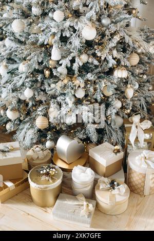 Wunderschön gewickelte Weihnachtsgeschenke in Gold und weiß, verziert mit Bändern und festlichen Dekorationen, platziert unter einem Milchbaum. Warm Stockfoto