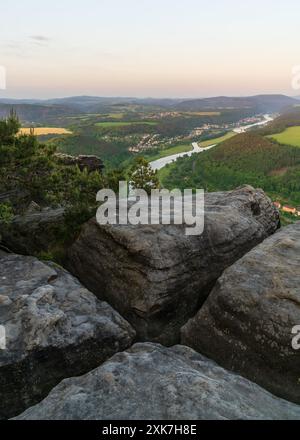 Herrlicher Blick durch den Felsen eines rustikalen Motivs mit grünen Wiesen und Feldern, gepflegten Häusern im Tal und der Elbe. Nationalpark Saxon Sw Stockfoto