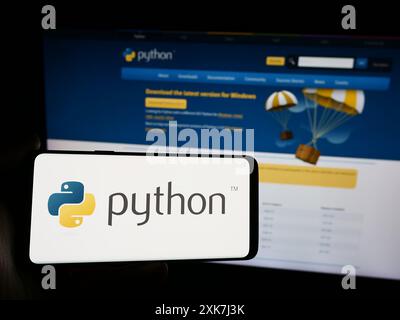 Person mit Smartphone und Logo der Organisation Python Software Foundation (PSF) vor der Website. Schwerpunkt auf dem Display des Telefons. Stockfoto