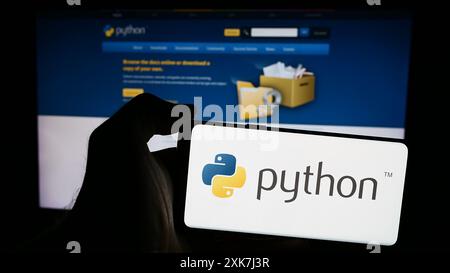 Person, die ein Mobiltelefon mit dem Logo der Organisation Python Software Foundation (PSF) vor der Webseite hält. Schwerpunkt auf dem Display des Telefons. Stockfoto