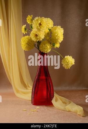 Strauß gelber Dahlien in einer roten Vase. Orangefarbener Hintergrund. Gelber Schal. Stillleben im Herbst. Stockfoto