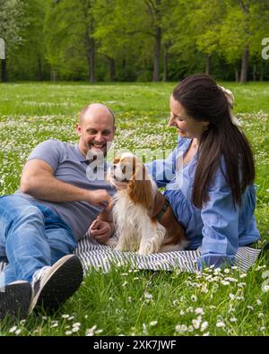 Glückliches schwangeres Paar verbringt Zeit zusammen auf einem Picknick draußen mit einem Haustier, Hund, Cocker Spaniel. Ich warte auf ein Baby, Liebes Stockfoto