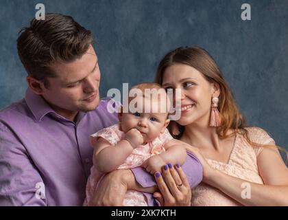 Frau und Mann, die ein Neugeborenes halten. Mom, Dad und Kind. Nahaufnahme. Porträt einer jungen lächelnden Familie mit einem Neugeborenen im Arm. Glückliche Familie auf der Ba Stockfoto