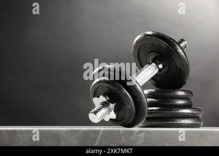 Barbell und Tellerstapel auf Marmortisch vor dunklem Hintergrund. Leerzeichen für Text Stockfoto