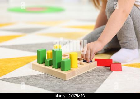 Kleines Mädchen, das mit geometrischen Holzfiguren auf dem Teppich spielt, Nahaufnahme. Kindergartenaktivitäten zur motorischen Entwicklung Stockfoto