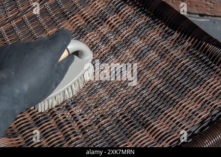 Person schrubbt Rattan-Patio-Stuhl mit einer Handbürste. Gartenheim Hausarbeit Chore Konzept. Stockfoto