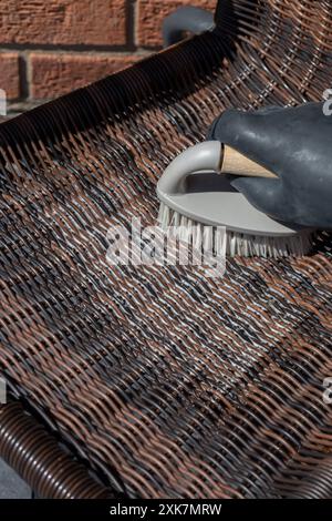 Person schrubbt Rattan-Patio-Stuhl mit einer Handbürste. Gartenheim Hausarbeit Chore Konzept. Stockfoto