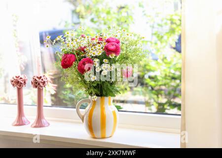 Wunderschöne Ranunkelblumen und Kamillen in Vase auf Fensterbank drinnen Stockfoto