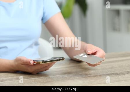 Frau mit SIM-Karte und Smartphone an Holztisch drinnen, Nahaufnahme Stockfoto