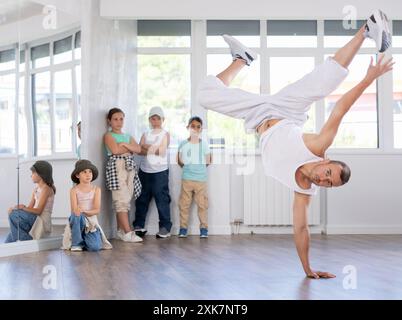 Sport männlicher Choreograf, der Unterricht im Tanzstudio führt, zeigt Gruppe von Kindern korrekte Durchführung choreografischer Übungen Stockfoto