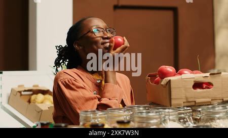 afroamerikanischer Käufer genießt frisches Aroma von Tomaten im Laden und riecht frisch geerntete Produkte, die in Kisten eines Supermarktes in der Nachbarschaft gelagert werden. Frau, die die lokale Landwirtschaft unterstützt. Kamera 1. Stockfoto