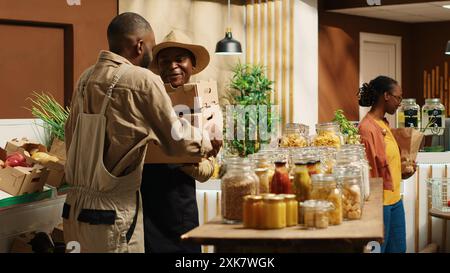 afroamerikanischer Lieferant, der dem Händler frische Produkte in Kisten gibt und an der Wiederauffüllung von Waren mit frisch geernteten Waren arbeitet. Landwirt und Lieferant arbeiten bei der Lieferung von Ladengeschäften zusammen. Kamera 1. Stockfoto