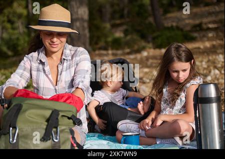 Mutter und Kinder bei einem Picknick, verbringen schöne Zeit zusammen in einem Wald. Sie wirken entspannt und glücklich und verbinden sich mit der Natur. Stockfoto