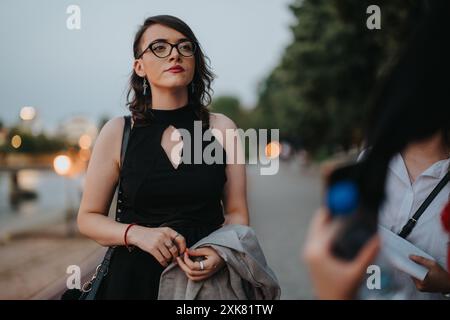 Selbstbewusste Geschäftsfrau in schwarzem Kleid und Brille, die in der Abenddämmerung draußen steht Stockfoto