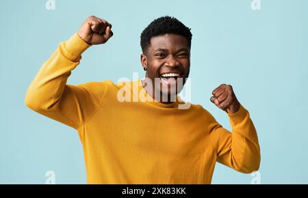 Emotionaler schwarzer Kerl, der die Fäuste auf Blau hochhebt Stockfoto