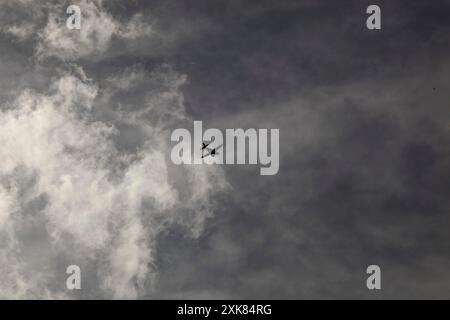 Ein kleines Propellerflugzeug, das hoch am Himmel vor einem grauen, runzelnden Himmel und weißen, rauchartigen Wolken fliegt. Ein düsteres Bild. Hochwertige Fotos Stockfoto