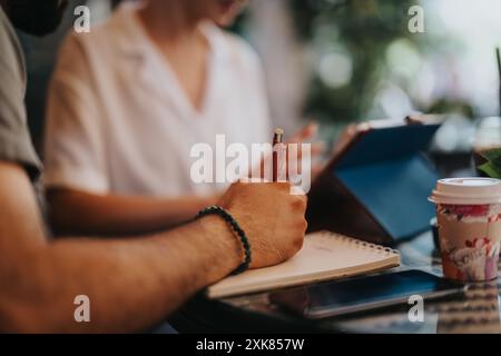 Geschäftstreffen im Café mit Personen, die Notizen machen und Tablets verwenden Stockfoto