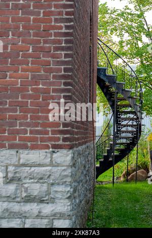 Das Äußere eines großen braunen Backsteingebäudes mit einem einzigen Glasfenster. Es gibt eine schwarze Metallspiraltreppe, die vom zweiten Stock zum G führt Stockfoto