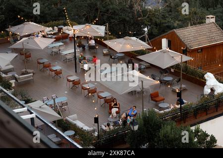 Navacerrada, Spanien. Juli 2024 Blick von oben auf das Café und die Terrasse des Restaurants am Abend. Die Leute entspannen sich auf der Terrasse eines modernen Hotels. Tische und Sitzplätze. Stockfoto