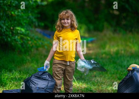 Kind mit Abfallbeutel und Müllzange während der Müllsammlung. Niedliches Kind mit Papierkorb, das Plastikmüll im Wald oder Park sammelt. Eco Stockfoto