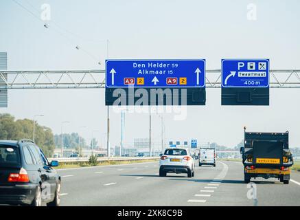 Den Helder, Niederlande - 27. August 2019: Ein klarer Blick auf eine Autobahn mit einem blauen Straßenschild, das Wegbeschreibung nach den Helder und Alkmaar anzeigt. Fahrzeuge werden auf der Straße unterwegs gesehen, und die Szene fängt das Wesen eines typischen Tages auf einer niederländischen Autobahn ein. Stockfoto