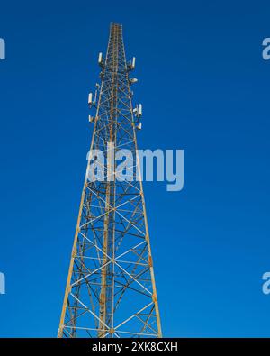 Aus der Nähe eines hohen Telekommunikationsturms mit weißen Antennen, der hoch in einen klaren blauen Himmel reicht. Stockfoto