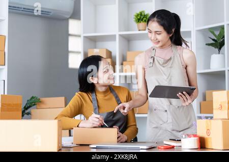 Zwei junge Unternehmerinnen arbeiten in einem modernen Büro mit Verpackungsboxen und digitalem Tablet zusammen Stockfoto