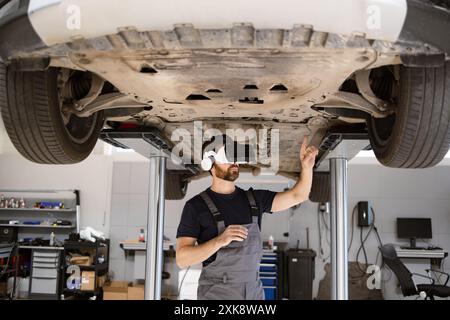 Mechaniker mit virtuellen Gläsern, um das Fahrzeug im Aufzug in der Garage zu inspizieren Stockfoto