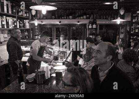 Gäste am Theken servieren die Mitarbeiter in einer kleinen Cicchetti Bar mit Wänden, die mit Whisky- und Weinflaschen gesäumt ist und in Dorsoduro, Venedig, Italien, verkauft werden kann Stockfoto