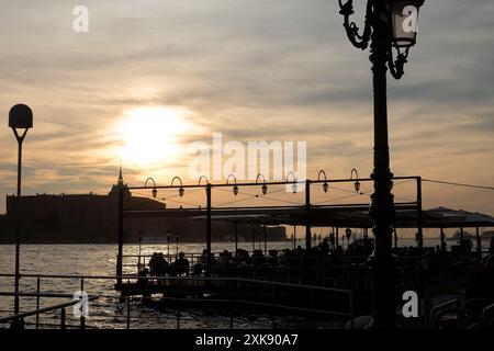 Ein Restaurant am Wasser auf einem Ponton am Giudecca Kanal, Dorsoduro Silhouette bei Sonnenuntergang, ein Sommerabend in Venedig, Italien Stockfoto