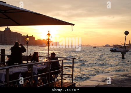 Ein Paar genießt einen spektakulären orangen Sonnenuntergang und abendliche Drinks in einem Restaurant im Freien am Wasser in Dorsoduro, Venedig, Italien Stockfoto