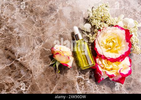 Kosmetikprodukt, Serum, Öl in einer Flasche mit einem Tropfer auf braunem Marmorhintergrund mit bunten Rosen. Ein Kopierbereich. Draufsicht Stockfoto