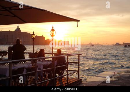 Ein Paar genießt einen spektakulären campari-Sonnenuntergang und abends Drinks in einem Restaurant im Freien am Wasser in Dorsoduro, Venedig, Italien Stockfoto