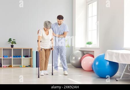 Ein Rehabilitationsspezialist in einer Klinik hilft einer älteren Frau, auf Krücken zu gehen Stockfoto