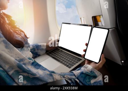 Frau, die im Flugzeug sitzt und ein Modell-Telefon hält. Geschäftsreisen, Reisen und Arbeit. Frau mit Smartphone und Laptop. Einsatz von Reise- und Luftfahrttechnologie Stockfoto