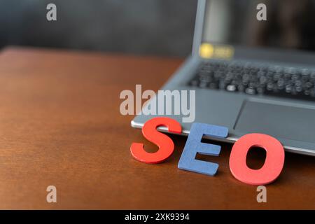 Wooden Letter steht für SEO-Abkürzung, die auf dem Laptop am Schreibtisch liegt. Modernes Marketing-Schlagwort SEO - Suchmaschinenoptimierung. Blick von oben auf Holztisch Stockfoto